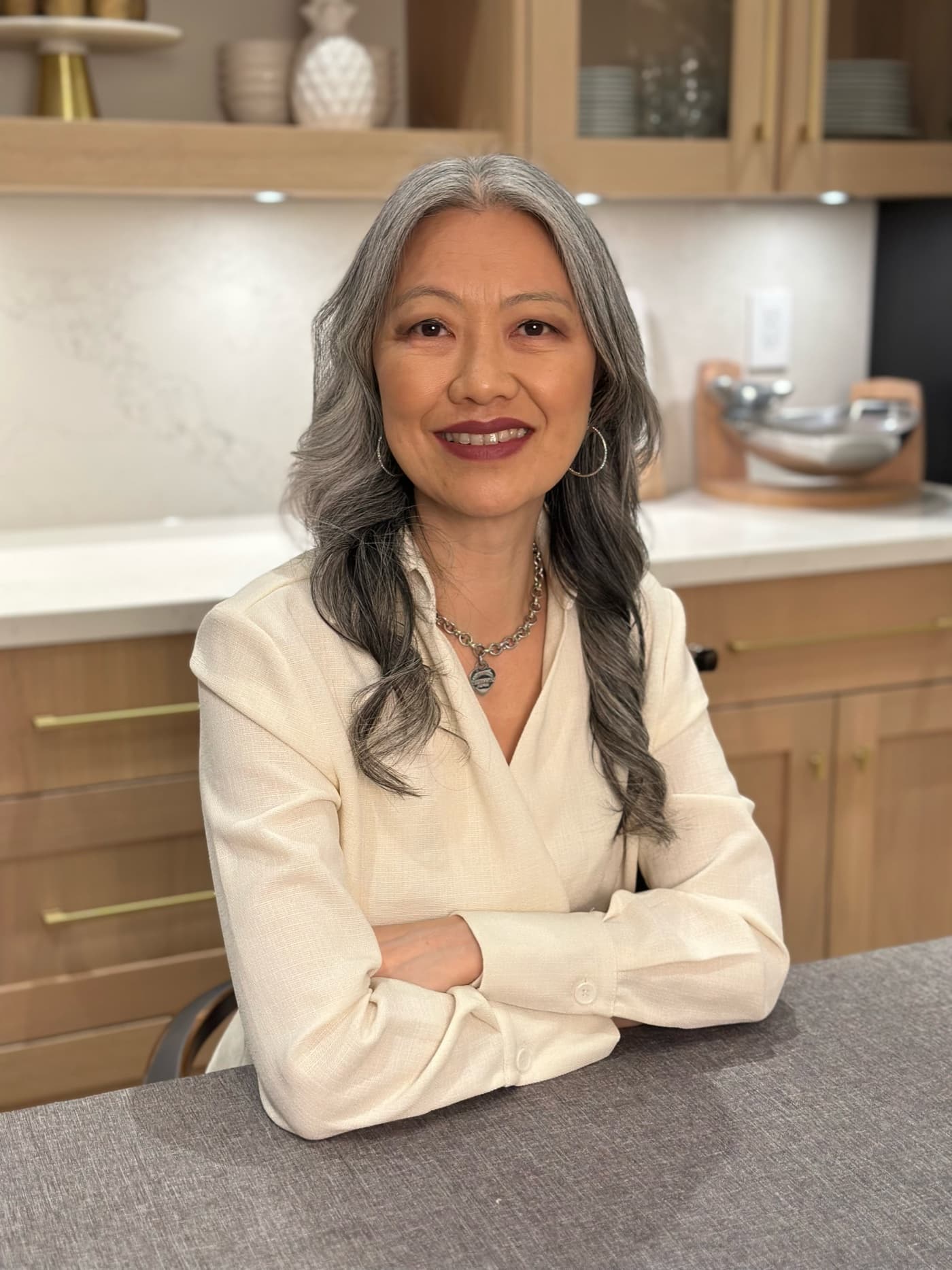 Stacey Tam, founder of Skola, smiling with her arms folded at a table